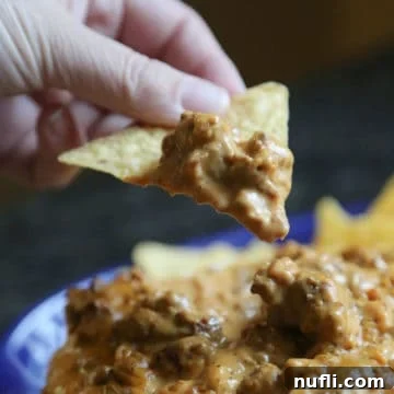 Hearty Meat Lover's Crockpot Queso Dip 5 Meat Lovers Queso on a tortilla chip above a bowl full of queso