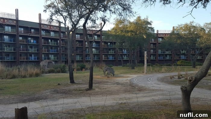Exterior view of Disney's Animal Kingdom Lodge at dawn, with a giraffe and zebras grazing on the foreground savannah