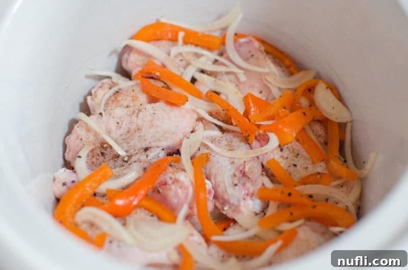 Spicy jerk chicken wings with vibrant red peppers and onions cooking in a white slow cooker, showcasing the slow cooking process