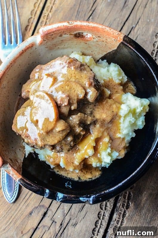 Salisbury steak over potatoes in a pottery bowl next to a fork