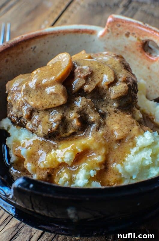 Salisbury steak over potatoes in a pottery bowl next to a fork