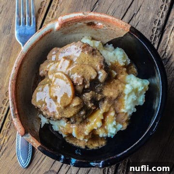 Salisbury steak over potatoes in a pottery bowl next to a fork