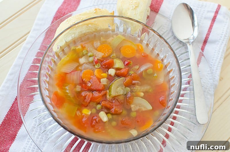 Vegetable soup in a glass bowl on a plate next to a spoon, inviting and rustic