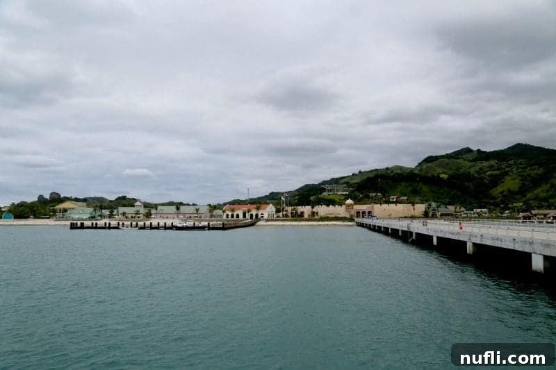 Long pier leading to buildings and a large grassy hill in Amber Cove