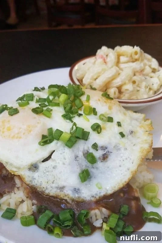 A hearty Loco Moco dish featuring a sunny-side-up egg, rich gravy, and mac salad served on a pristine white plate.