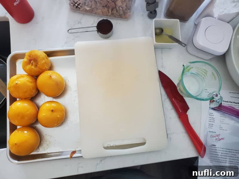 Luscious Crockpot Peach Butter 5 Prepared peaches on a baking sheet next to a cutting board and red knife.