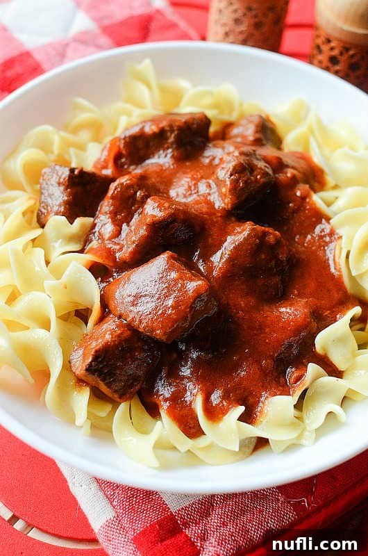 Set It and Forget It Goulash 3 Crockpot Goulash presented beautifully on a white plate, served alongside perfectly cooked egg noodles, showcasing its rich, savory appeal.
