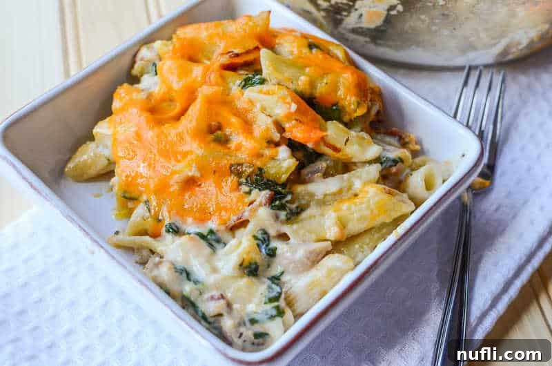 Large baking dish filled with cheesy pasta casserole, with a white bowl of the same dish and a fork beside it, ready to be served