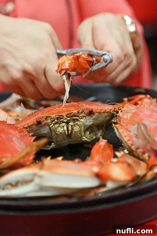 A hand expertly cracking a crab leg, with a whole crab visible below, illustrating the interactive dining experience.