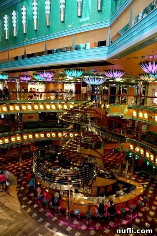 The dazzling Carnival Magic atrium, featuring grand stairs leading to the lower level and illuminated by fun, colorful lights, creating a lively central hub.