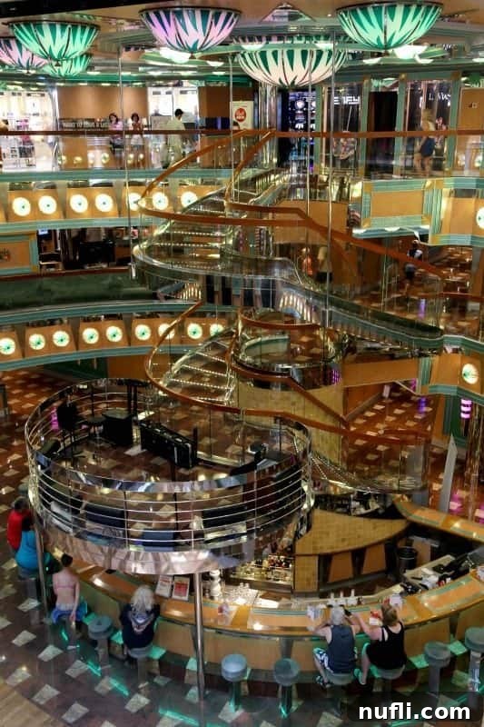 The elegant Carnival Magic lobby with a clear, inviting staircase leading down to a sophisticated bar area, perfect for pre-dinner drinks.