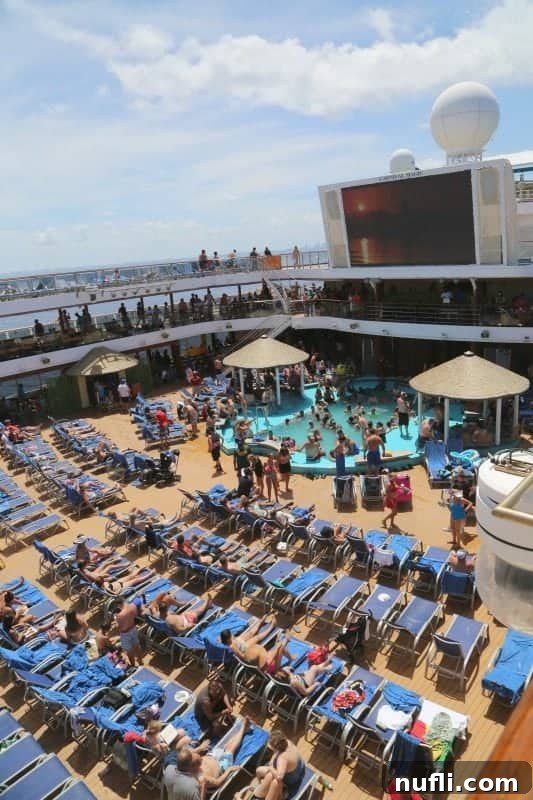 Looking over the vibrant Lido Deck of the Carnival Magic with blue lounge chairs and outdoor pool, beckoning guests to relax and play.