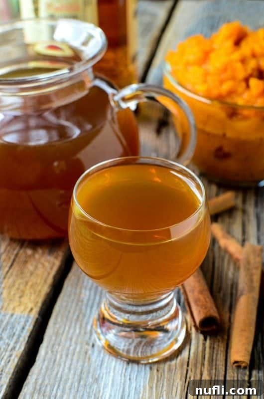 Cozy Slow Cooker Pumpkin Spice Liqueur 3 Small glass of Pumpkin Spice Liqueur on a wood background with cinnamon sticks, a bowl of pumpkin puree, and pitcher