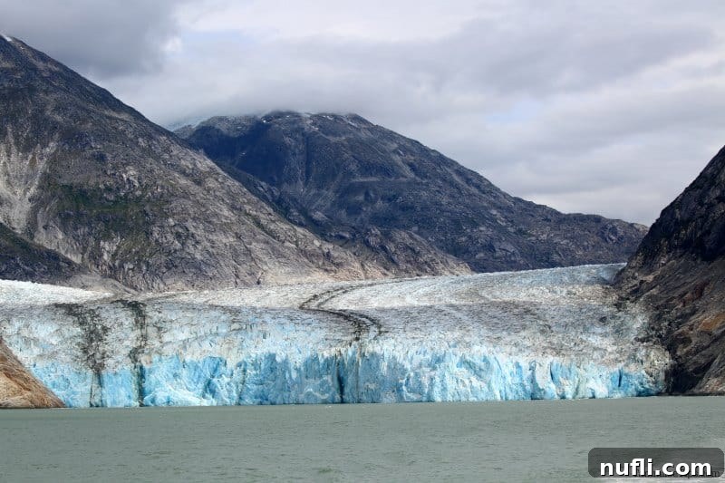 Glacier with streaks at the end of the water with mountains in the background. 