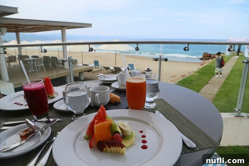 Table with white dishes near a glass balcony and the Bay of Banderas in the background, a luxurious dining setting.