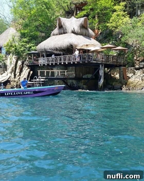 Live Love Grill boat near a restaurant over the water with a thatch roof, accessible only by sea.
