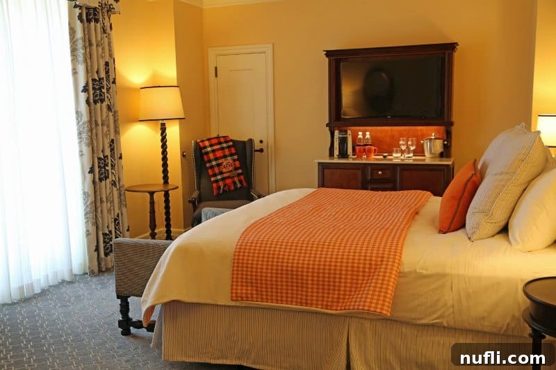 Oklahoma State University's Atherton Hotel in Stillwater 3 Luxurious bed at The Atherton Hotel featuring soft white linens, a warm orange throw blanket, and an inviting armchair next to a lamp.