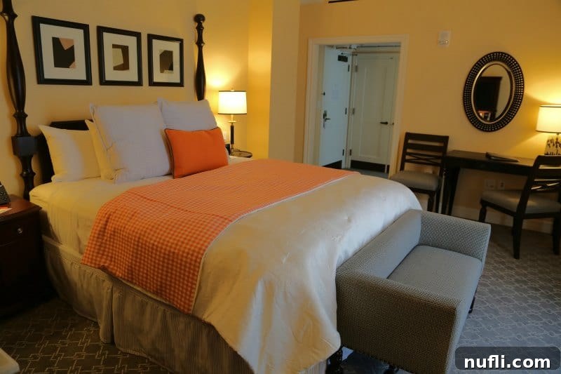 Oklahoma State University's Atherton Hotel in Stillwater 4 Close-up of a plush bed at The Atherton Hotel with a decorative orange throw blanket and multiple soft pillows, highlighting the luxurious bedding.