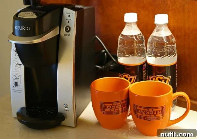 Oklahoma State University's Atherton Hotel in Stillwater 5 Elegant orange coffee mugs next to a Keurig coffee maker, ready for a warm beverage at The Ranchers Club, showcasing the attention to detail.