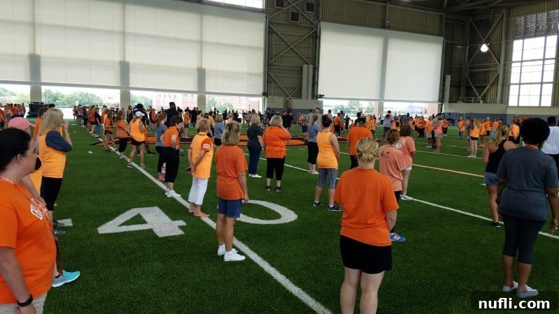 Group of women in orange shirts spread across a football field, participating in drills at Football 101.