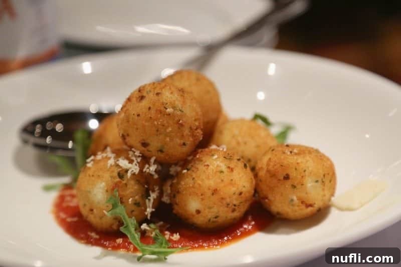 Golden-fried Arancini balls, perfectly arranged on a pristine white plate, showcasing their inviting texture and delicious appeal.