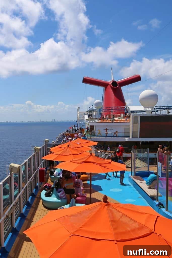 Outside seating under orange umbrellas on the upper deck near the Carnival Funnel