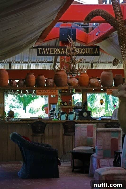 A rustic wooden sign for 'Taverna Tequila' hanging above an inviting outdoor seating area at a restaurant