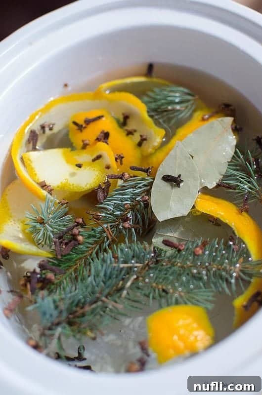 Orange slices, pine needles, and whole cloves simmering in water in a white crock pot, creating a festive Christmas potpourri.
