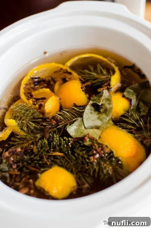 A white slow cooker filled with orange peels, pine needles, and water, simmering to create a wonderful Christmas scent for the home.