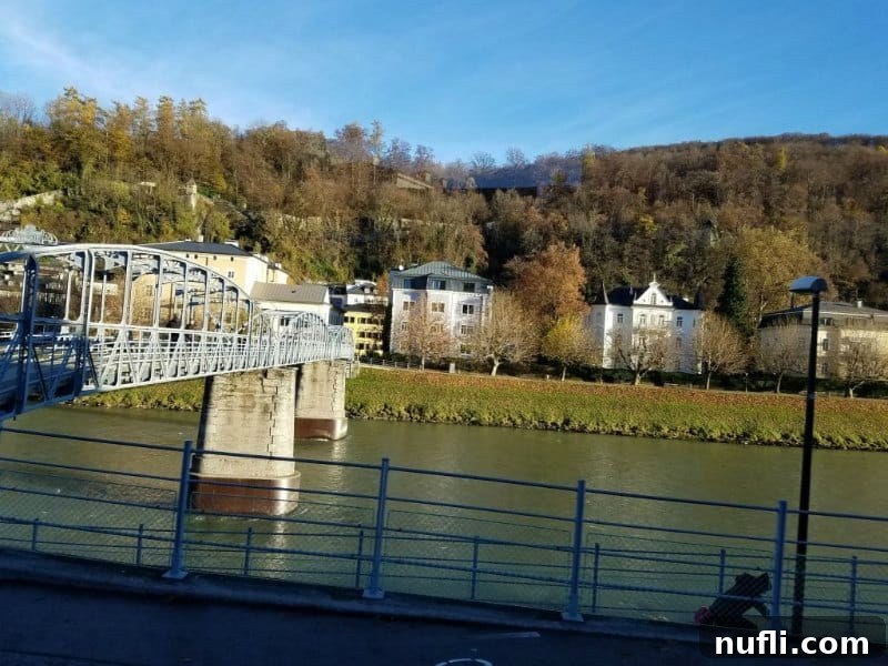 A picturesque bridge spans a river, flanked by charming houses and rolling hills along the water's edge.