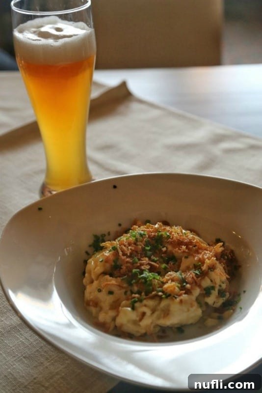 Germany: Where I Found What My Life Was Missing 3 Delicious Cheese Spaetzle in a white bowl, garnished with crispy fried onions, alongside a tall glass of refreshing German beer