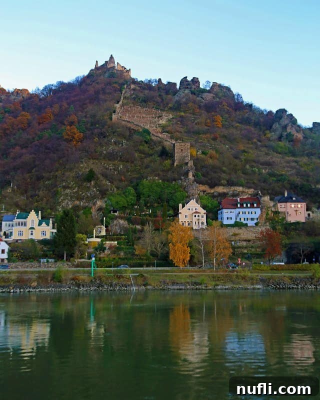 Cruising Austria's Wachau Valley with Viking 7 Panoramic view across the Danube river to colorful buildings and an ancient castle high on the hillside in Wachau Valley