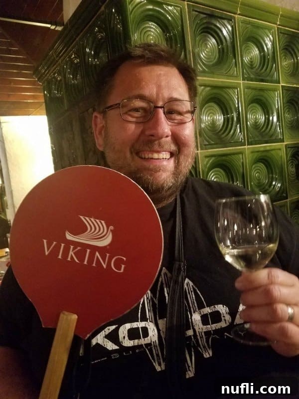 John holding a Viking River Cruise sign and a wine glass at a Heurigen event