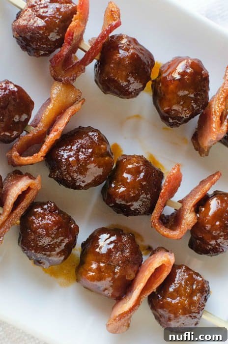 Bacon Bourbon Slow Cooker Meatballs 3 Individual Bacon Bourbon Meatball skewers featuring a meatball, a folded piece of crispy bacon, and another meatball, arranged on a pristine white serving dish.