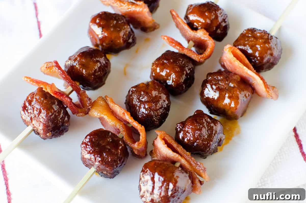 Bacon Bourbon Slow Cooker Meatballs 5 A top-down view of skewered Bacon Bourbon Meatballs on a large white platter, showcasing their glistening sauce and crisp bacon.
