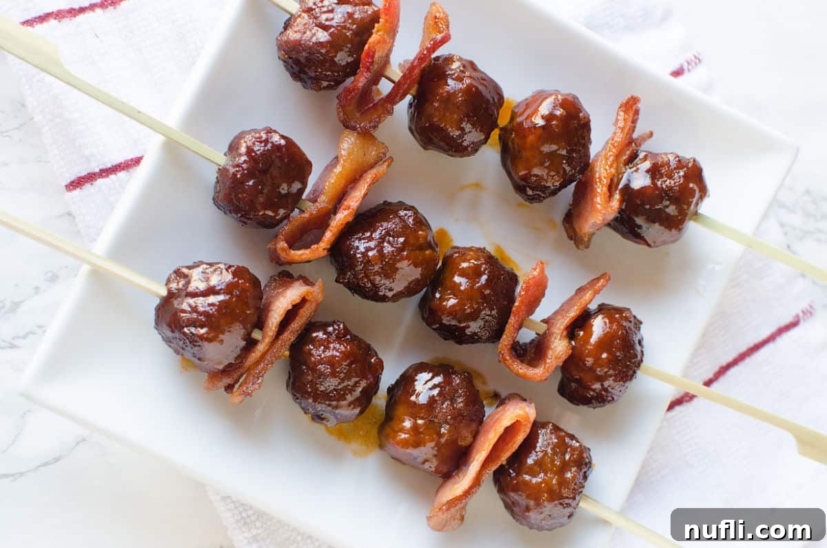 Bacon Bourbon Slow Cooker Meatballs 6 Close-up of a single Bacon Bourbon Meatball skewer with a folded piece of bacon, resting on a white plate, highlighting the delicious glaze.