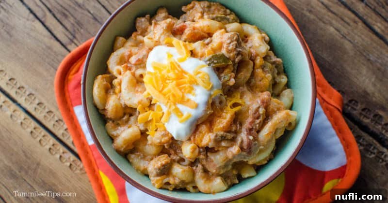 Crockpot taco pasta with sour cream and cheese on top in a bowl sitting on an orange potholder