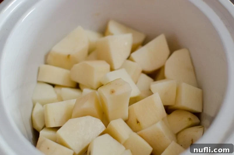 Decadent Slow Cooker Loaded Mashed Potatoes 3 Cubed potatoes in a white slow cooker bowl