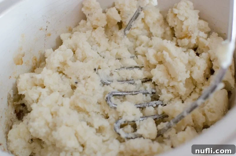 Decadent Slow Cooker Loaded Mashed Potatoes 5 Potato masher mashing potatoes in a slow cooker