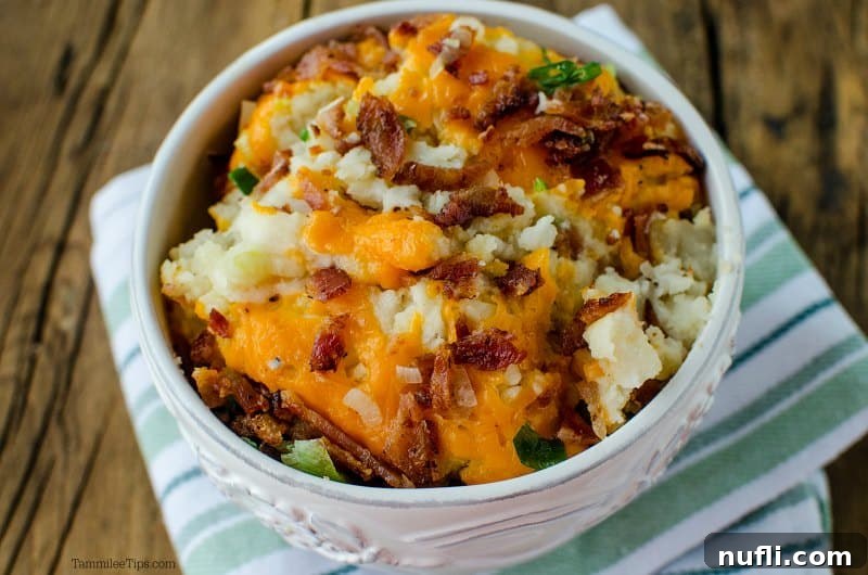 Decadent Slow Cooker Loaded Mashed Potatoes 8 White bowl filled with mashed potatoes, cheese, green onions, and bacon.