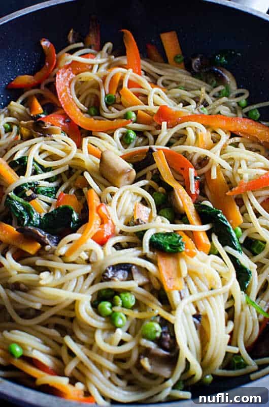 Close-up of lo mein noodles and mixed vegetables simmering in a large pan, ready to be tossed with sauce.
