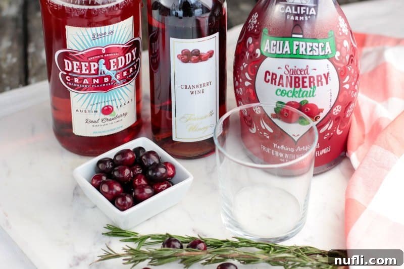 Ingredients for a Spiced Cranberry Cocktail including cranberry vodka, cranberry wine, and spiced cranberry juice, beside fresh cranberries and a cocktail glass.