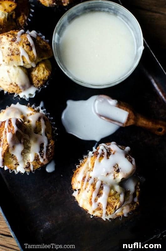 Close-up of golden brown maple monkey bread bites drizzled with icing on a dark serving platter, with a small bowl of extra icing in the background.