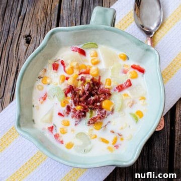 Bacon and corn chowder in a ceramic bowl next to a spoon on a cloth napkin