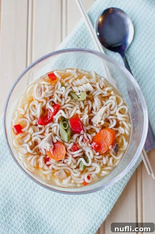 A steaming bowl of Slow Cooker Chicken Ramen Soup, garnished with fresh herbs, sits on a cloth napkin next to a spoon, inviting comfort.
