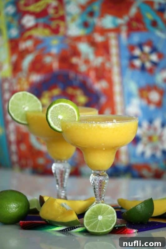 yellow margaritas in margarita glasses with lime wheels and mangos