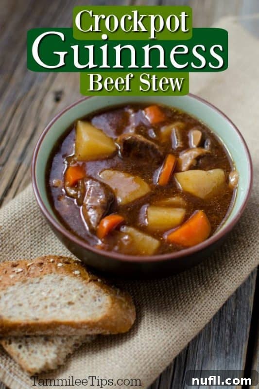 A bowl of rich, dark Crockpot Guinness Beef Stew with tender beef chunks, carrots, and potatoes, served with two slices of crusty bread on the side.