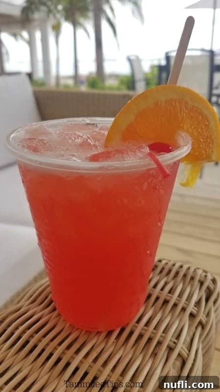 Vibrant tropical cocktail with an orange slice and cherry garnish, set against a blurred beach background