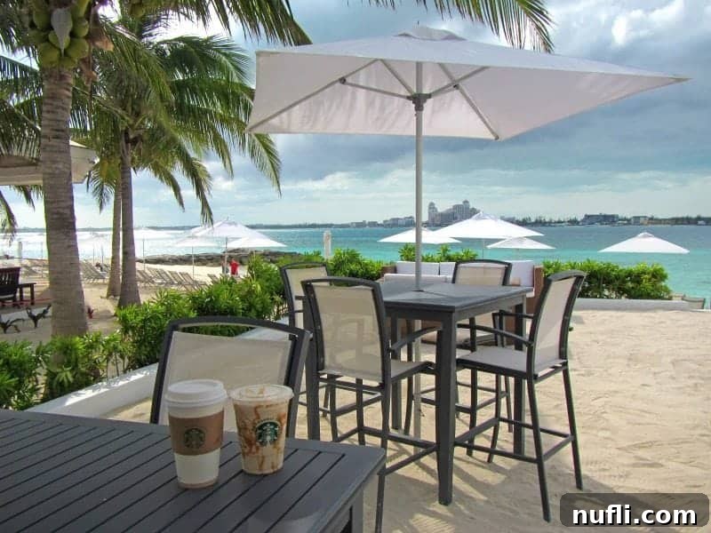 Starbucks cups on a table next to tall table with white umbrella, overlooking the beach