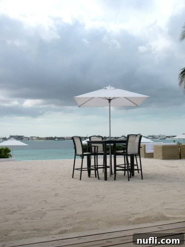 Tall table with white umbrella in the sand, tropical waters and distant shore in the background